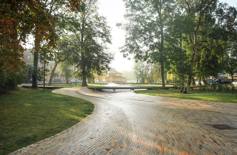Patterned brick paving in a public plaza with trees and benches under soft morning mist