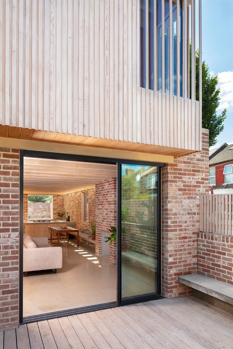 Sliding glass door opening from timber deck into living space with exposed brick walls and timber soffit