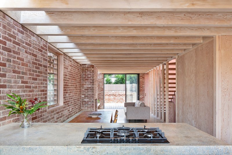 Open kitchen with exposed timber joists above concrete counter and gas cooktop facing brick walls
