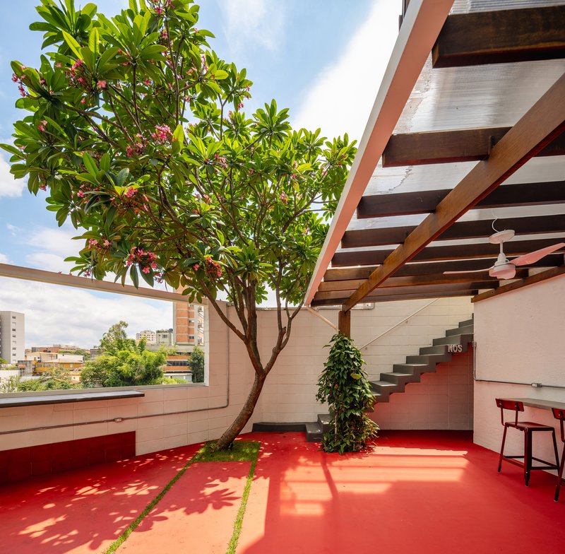 Open-air courtyard showing timber pergola, floating staircase, and flowering tree casting shadows on red flooring