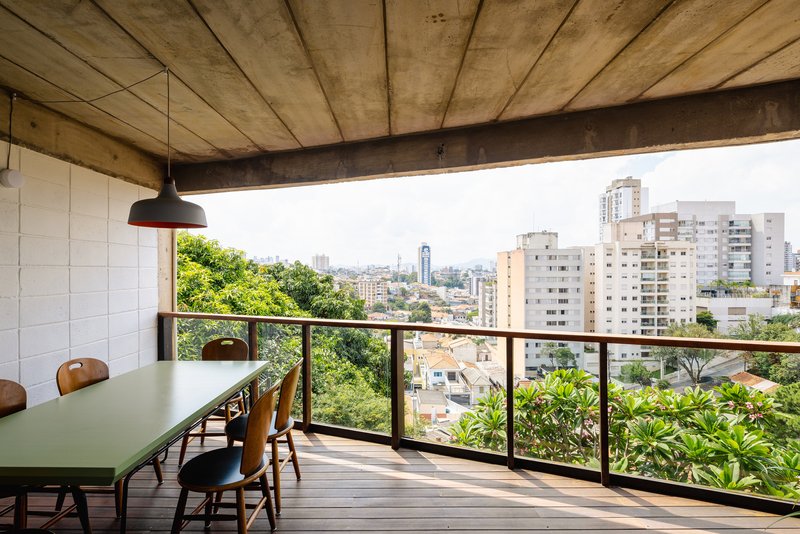 Dining terrace with timber decking and metal railing overlooking a green neighborhood and distant towers