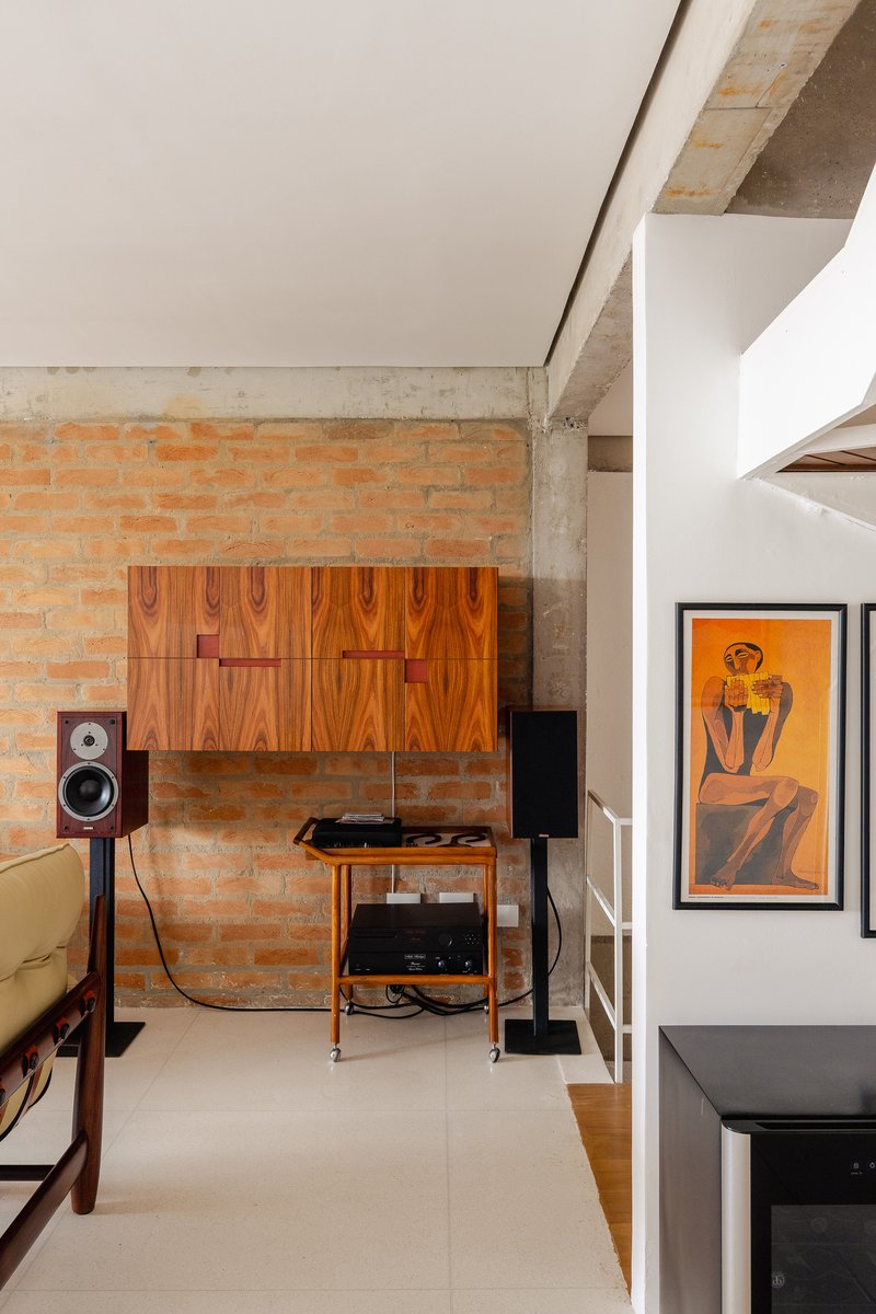 Exposed brick wall with wood veneer cabinet panels and concrete beam above pale tile flooring