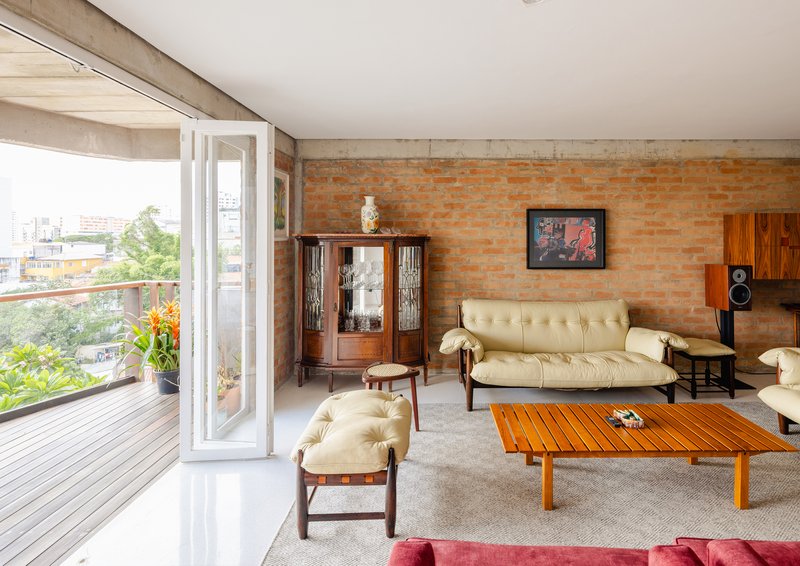 Living room with exposed brick wall, folding glass doors opening to timber deck overlooking greenery