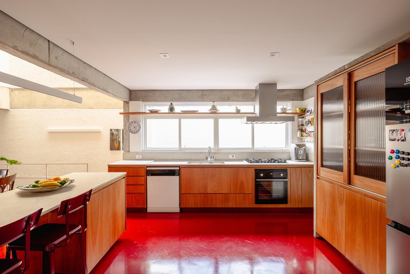 Kitchen galley with wood cabinetry and stainless appliances on a bright red resin floor