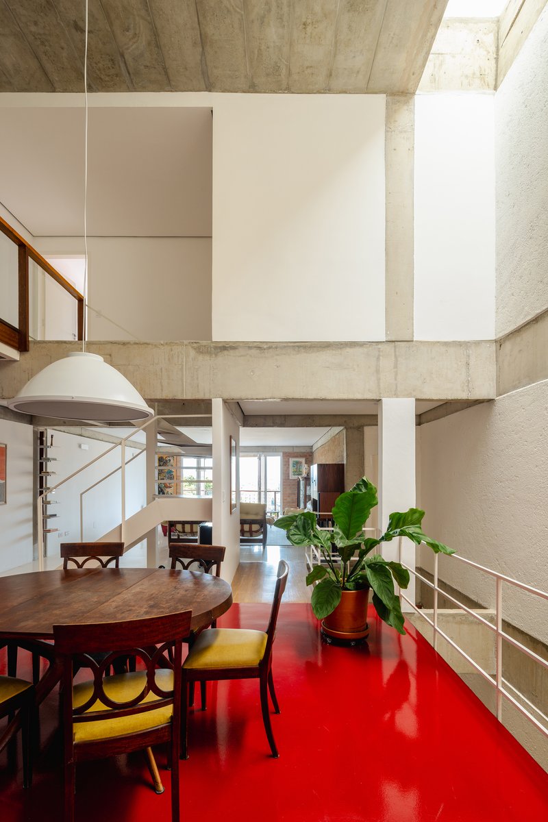 Double-height dining area with red resin floor, exposed concrete beams, and potted banana plant