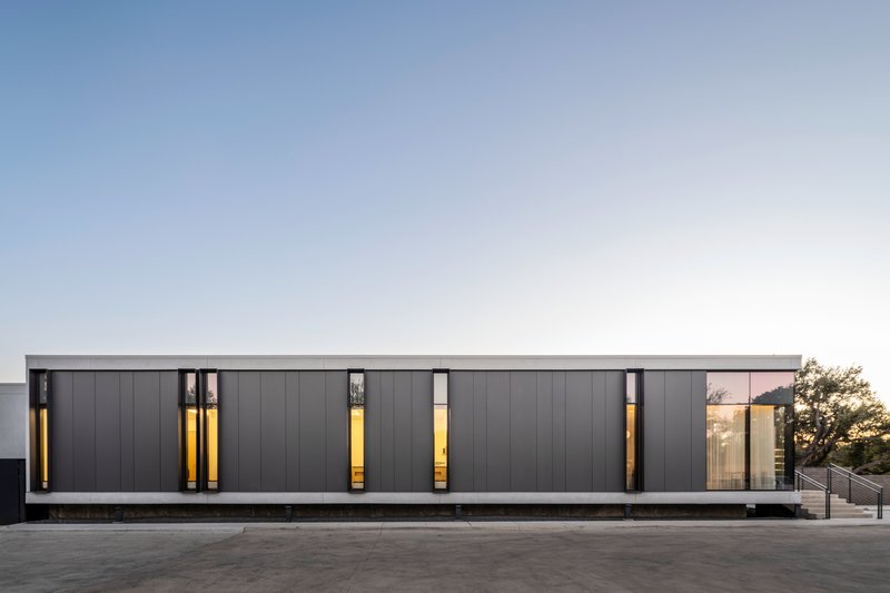 Street facade with dark metal panels and vertical window slits illuminated at dusk