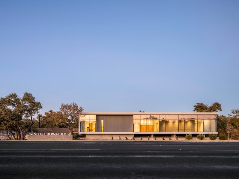 Front elevation showing the low horizontal volume with illuminated interior at dusk