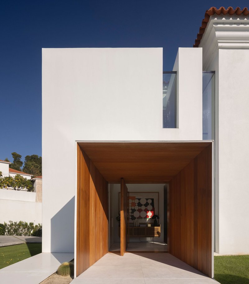 Recessed entry portal clad in timber with pivoting door opening to the interior under clear blue sky