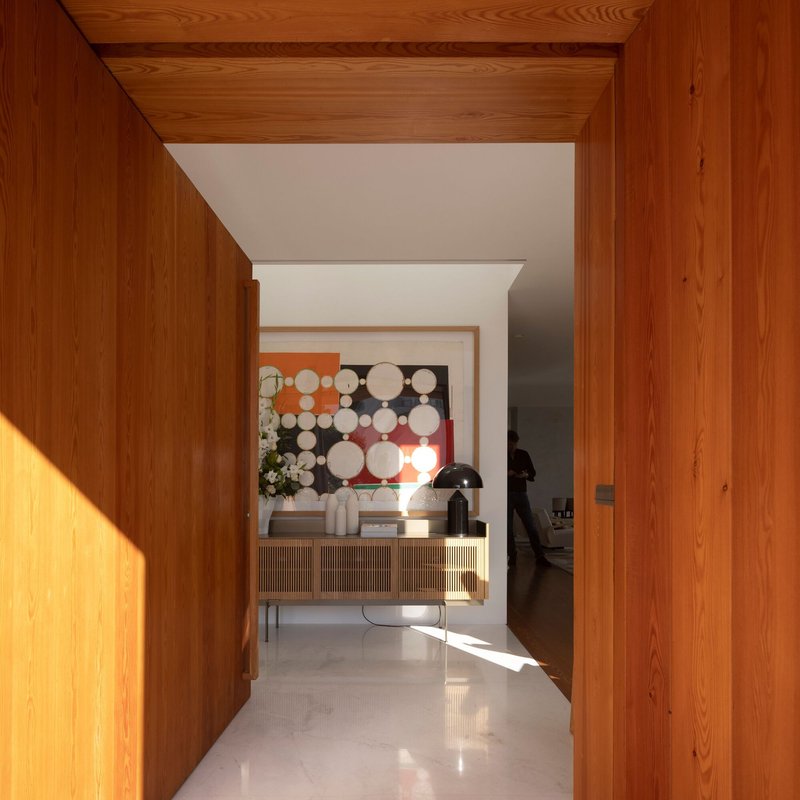 Timber-lined entry corridor with polished white floor leading to an interior with artwork and console