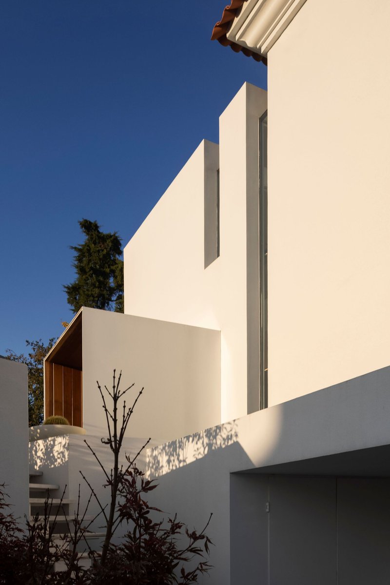 White stucco facade with stepped volumes and a narrow vertical window under a clear blue sky