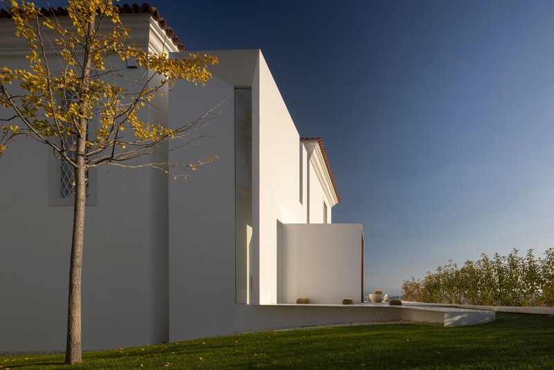 White rendered volumes beside a lawn and tree with autumn foliage at dusk