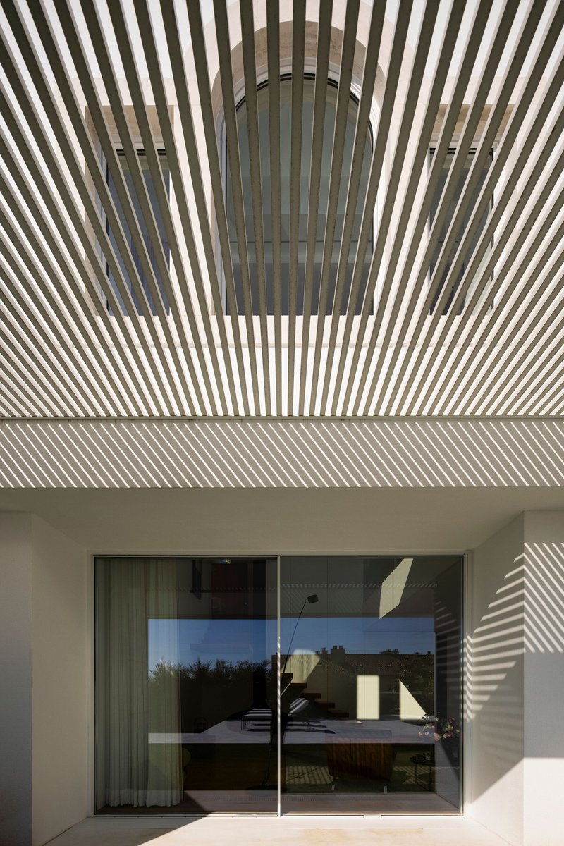 Timber slat pergola casting striped shadows on the wall and glass door below