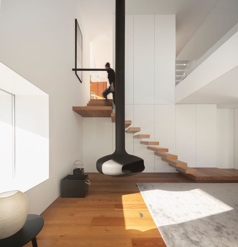 Floating timber staircase with glass balustrade and suspended black fireplace as figure ascends