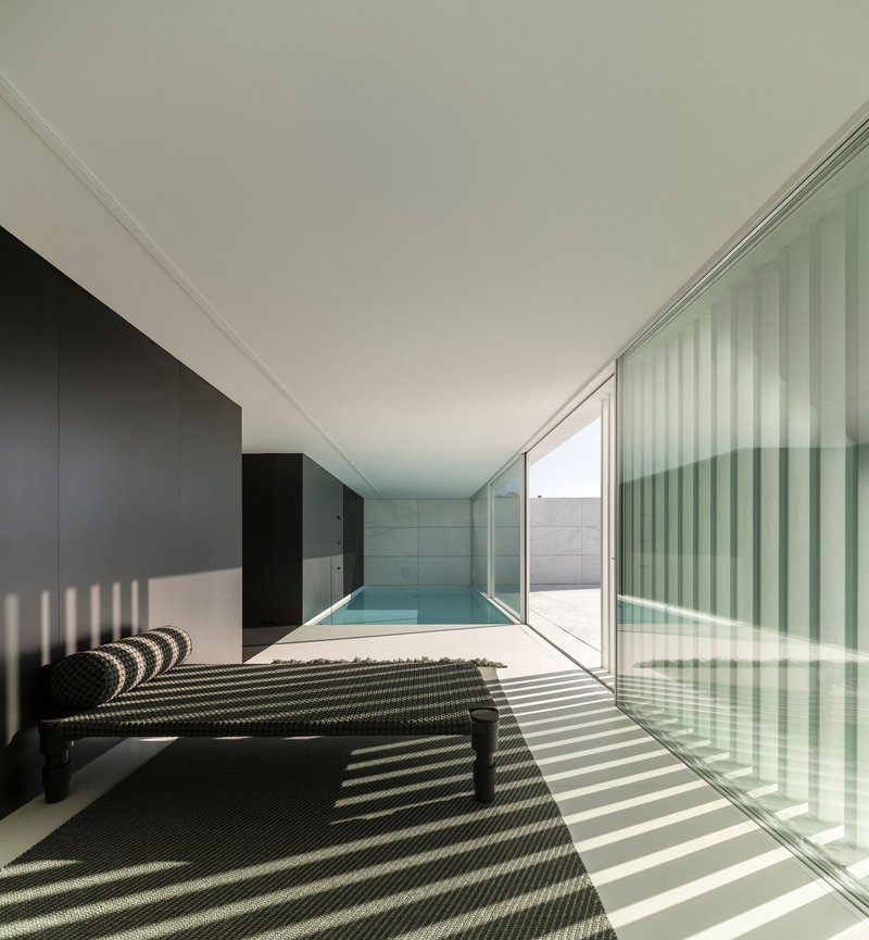 Indoor pool chamber with vertical pleated glass screens casting striped shadows across black tile floor