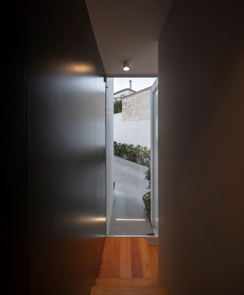 Timber staircase descending toward a doorway opening onto a white courtyard with planted greenery
