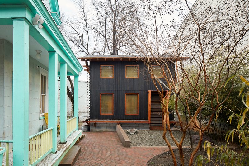 Two-story dark timber-clad volume with square windows seen from a turquoise porch across bare trees