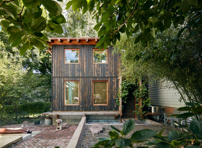 Front facade of vertical charred wood siding with four symmetrical windows framed by garden foliage
