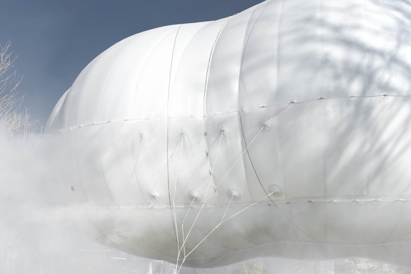 Close-up of the tensioned white membrane surface with tether lines and seams under a cloudy sky