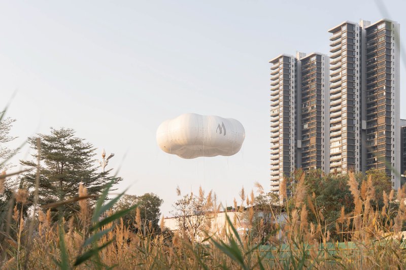 Airborne white fabric balloon floating above ornamental grasses with residential towers in the distance