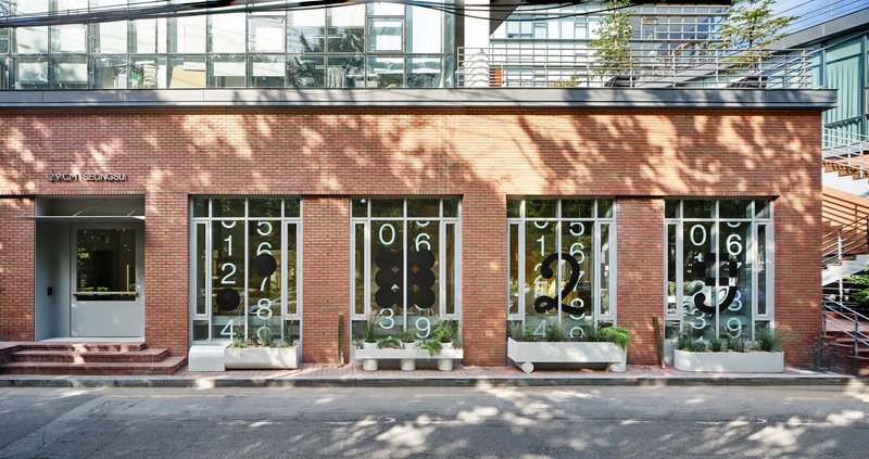 Red brick facade with tall windows overlaid by white numeric patterns and dappled tree shadows