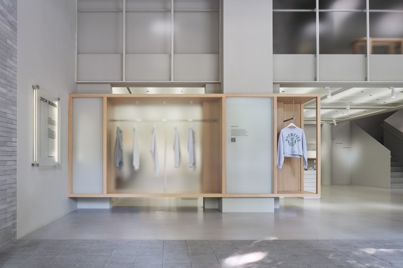 Wall-mounted display box in light wood with frosted glass doors and merchandise inside
