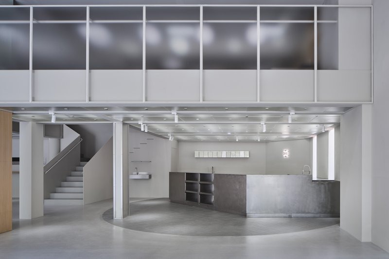 Ground floor sales area with curved counter, floating staircase, and suspended mezzanine framed by white columns