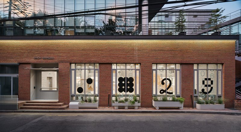 Red brick facade with large storefront windows displaying oversized graphic numerals at dusk