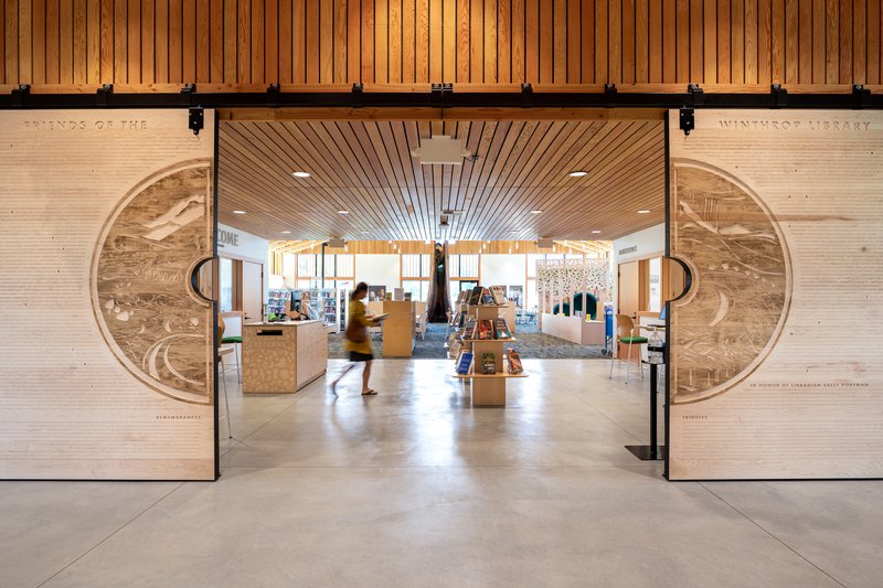 Sliding barn doors with circular wood grain panels opening to library interior with patron in motion