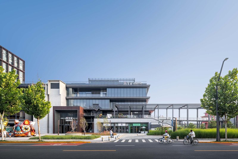 Street view of the layered glass facade with cyclists passing and a ceremonial lion sculpture on the corner