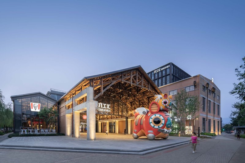Timber truss pavilion with concrete columns and a painted mascot sculpture at the entrance plaza