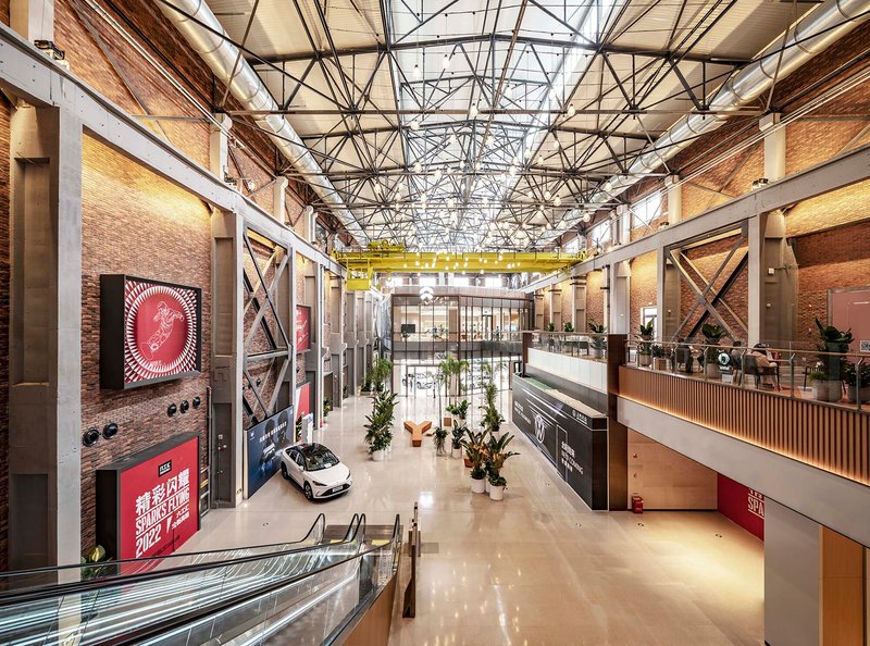 Interior hall with exposed steel trusses, brick walls, mezzanine levels and a display car on polished floor