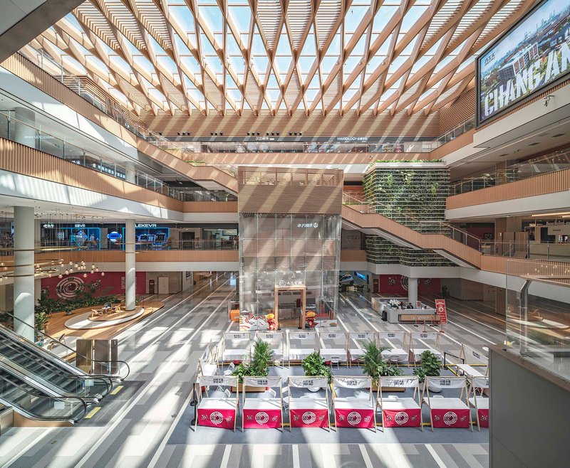 Multi-story atrium with timber lattice skylight casting diagonal shadows across the terrazzo floor below
