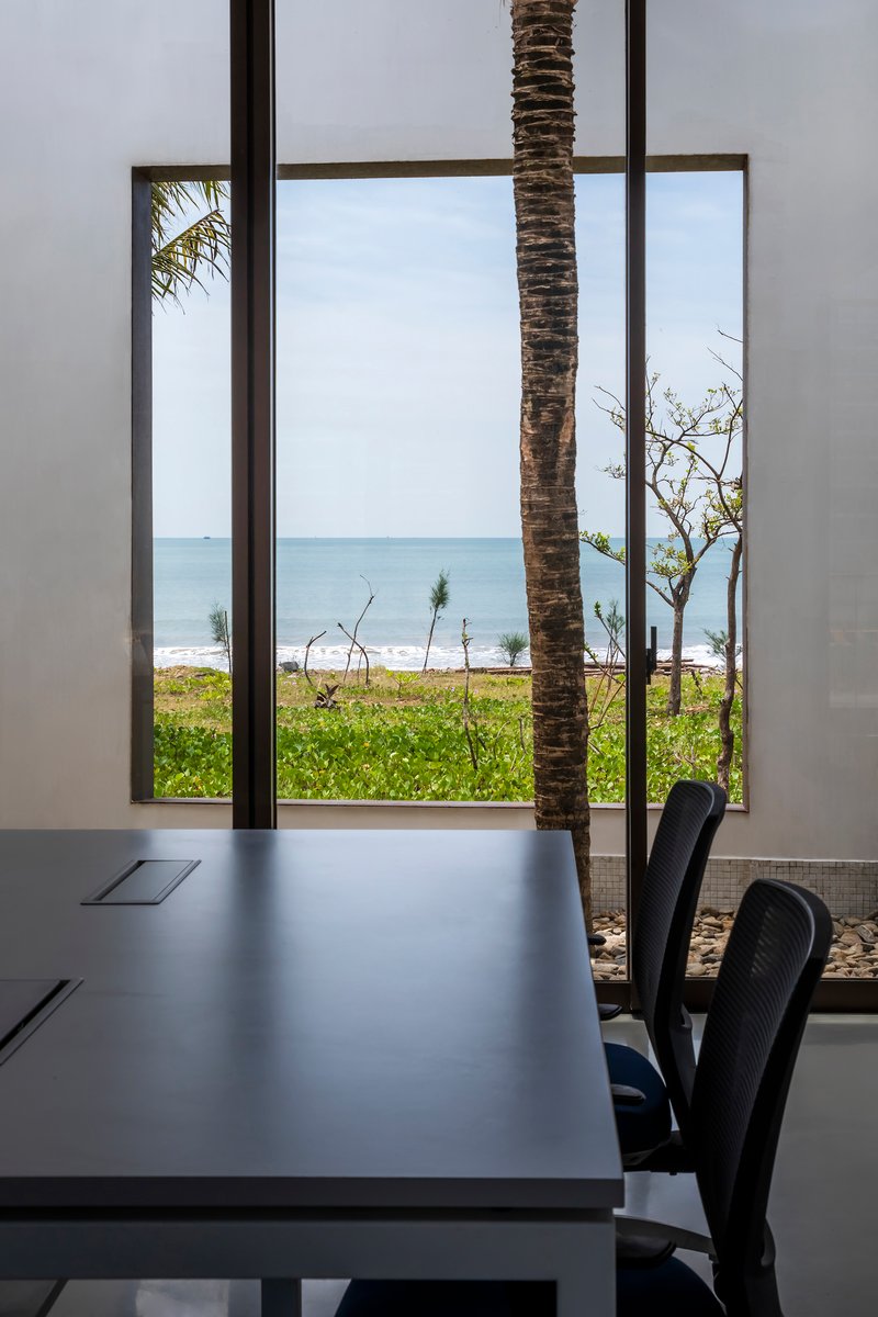 View through floor-to-ceiling window framing a palm tree trunk with ocean horizon beyond