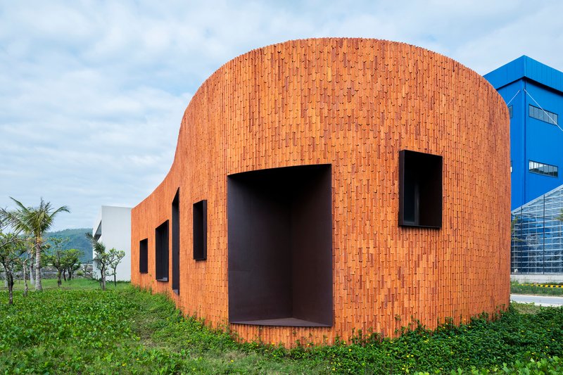 Curved brick facade with deep-set rectangular openings in a grassy field under cloudy skies