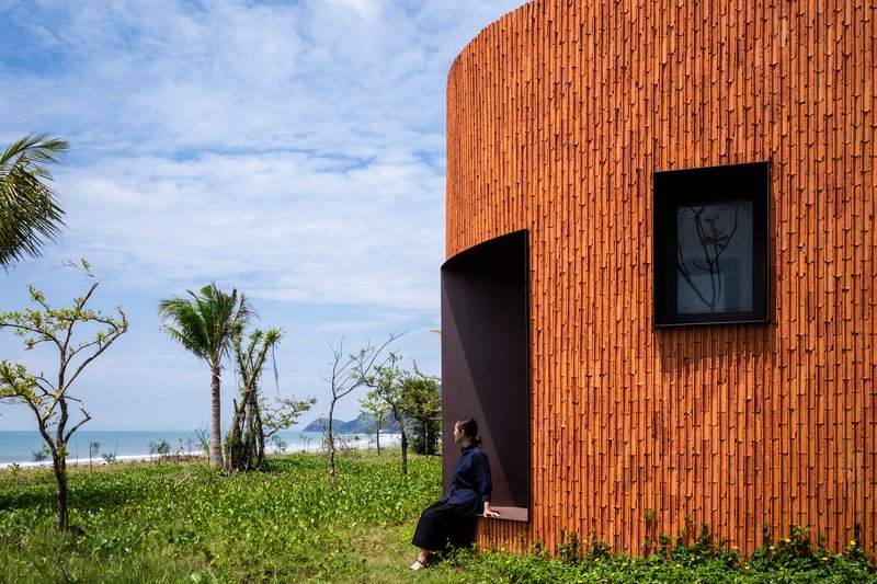 Figure seated on a metal bench protruding from the curved brick wall facing palm trees