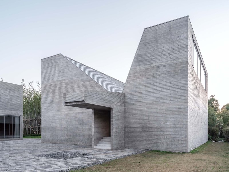 Entrance facade with cantilevered canopy and angled brick volumes flanked by bamboo and gravel paths