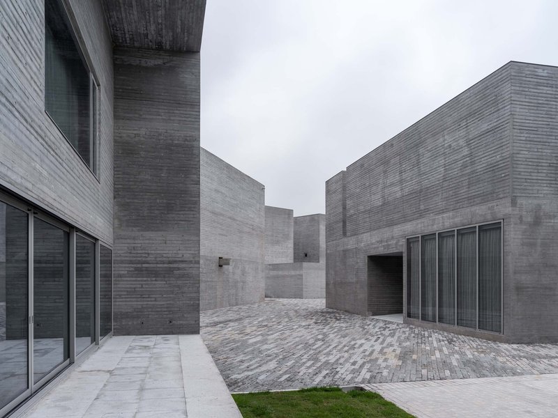 Concrete courtyard with brick paving surrounded by board-formed walls and glazed openings