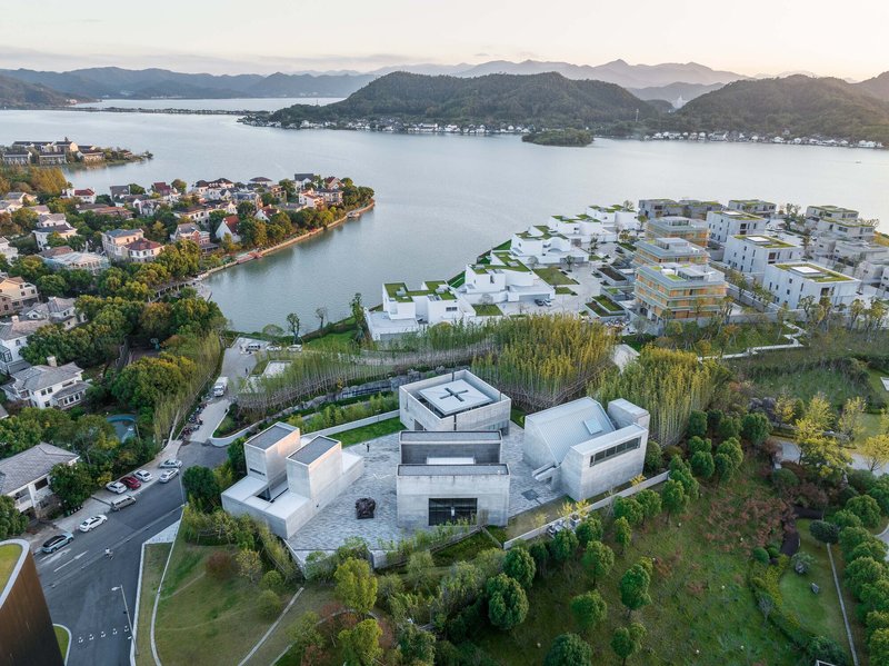 Drone view of the clustered white volumes among green landscape overlooking a lake and distant mountains at dusk