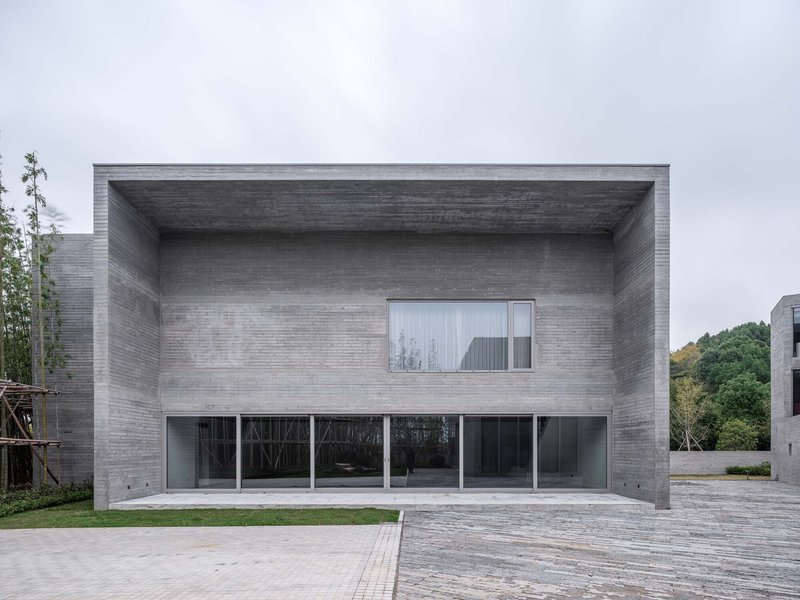 Deep recessed porch in horizontally banded concrete with upper window and ground-level glazing on wet pavement