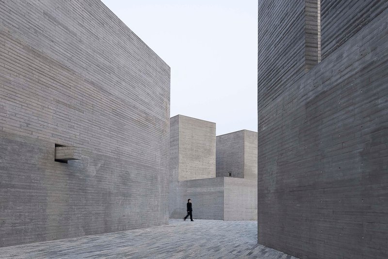 Narrow courtyard between stepped concrete block walls with a single figure walking through the space