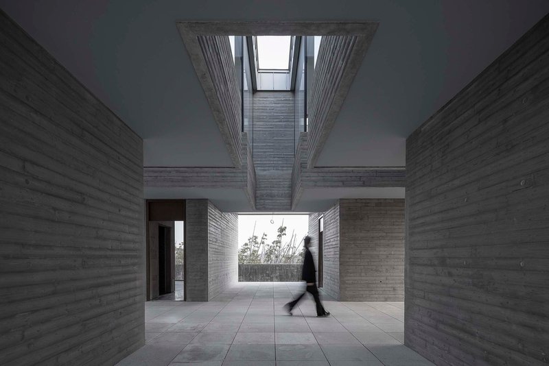 Interior courtyard with board-formed concrete walls, open skylight above, and a person in motion