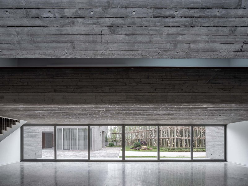 Interior with horizontal timber ceiling and floor-to-ceiling glazing overlooking a courtyard and birch grove