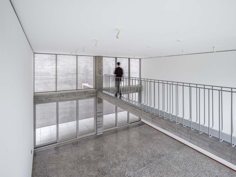 Upper-level bridge with metal railing overlooking the double-height space and exterior courtyard wall