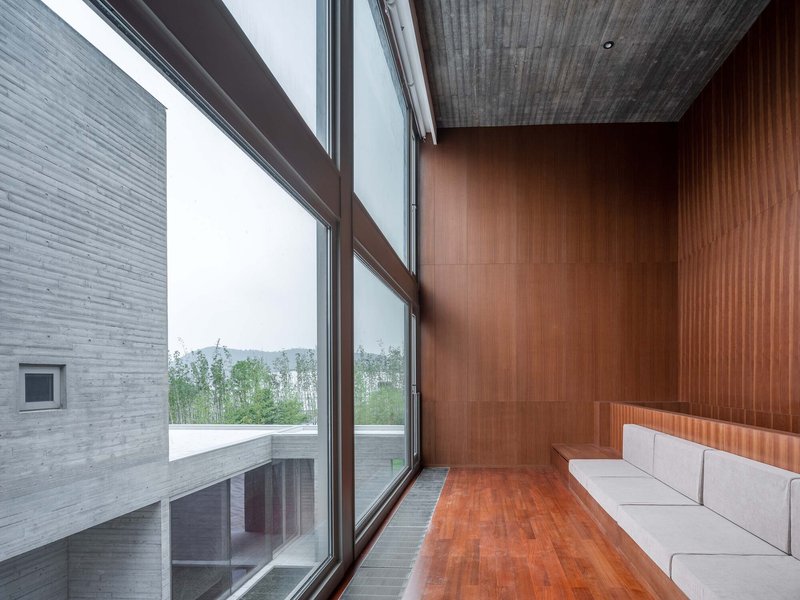 Room with timber ceiling and wall panels, tall windows, and built-in white seating on wood floor