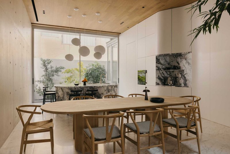 Dining area with oval timber table overlooking a planted courtyard through floor-to-ceiling glazing