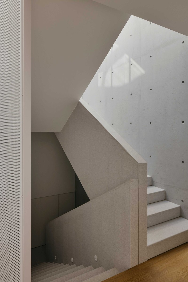 Concrete staircase with cantilevered treads beneath an angled skylight casting shadow patterns