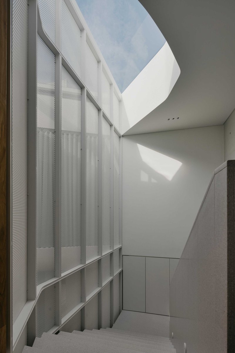 Interior courtyard with translucent perforated metal panels and an angular skylight opening to blue sky