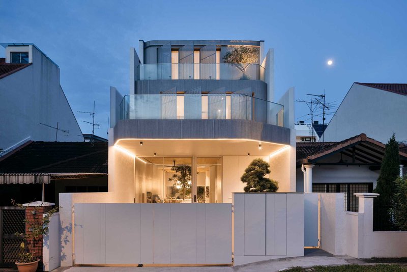Street view of the tiered white facade with perforated metal screening at dusk under moonlight