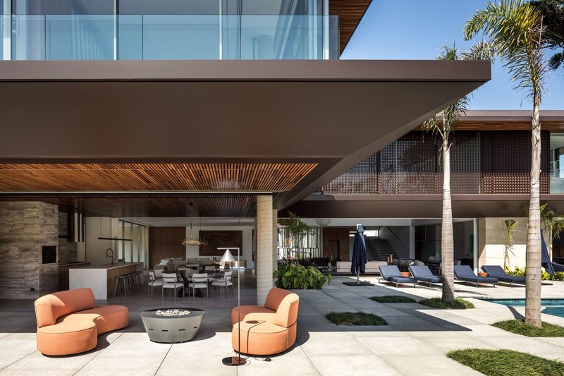 Covered outdoor terrace with timber slatted ceiling and stone columns opening to the poolside lounge area