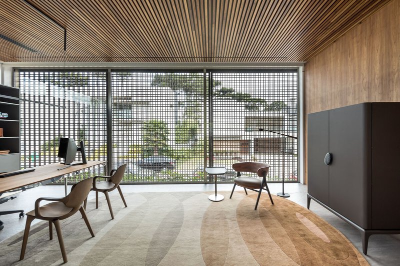 Interior study with radiating timber slat ceiling above a gridded metal screen wall opening to greenery